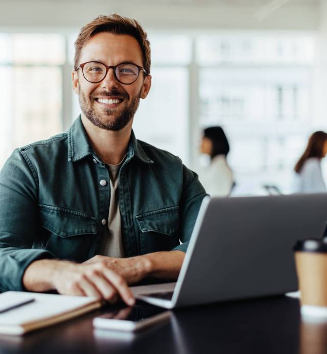 Portrait of a business man sitting in an office Portrait of a business man sitting in an office with his colleagues in the background. Happy business man working in a co-working office.
